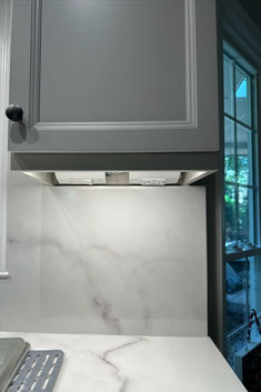 a kitchen with white marble counter tops and gray cabinets