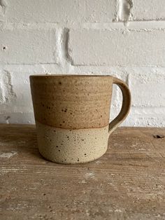 a coffee cup sitting on top of a wooden table next to a brick wall with white paint