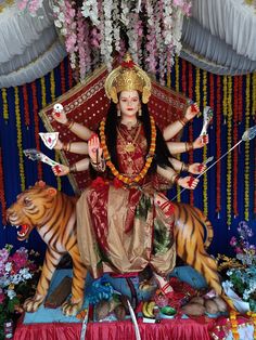 a statue of the hindu goddess sitting on top of a tiger in front of flowers