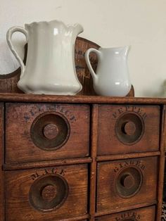 an old wooden dresser with two white pitchers on top