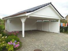 a white building with a black roof and flowers around it