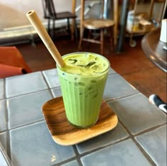 a green smoothie in a glass on a wooden plate with a bamboo straw sticking out of it