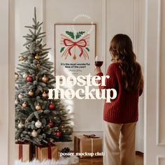 a woman standing in front of a christmas tree holding a wine glass with the words poster mockup on it