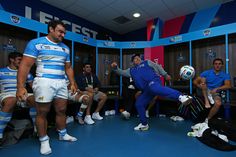 a man kicking a soccer ball in a locker room with other men around him watching