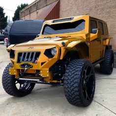 a yellow jeep is parked in front of a brick building with another vehicle behind it