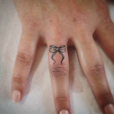 a woman's hand with a bow tattoo on her left thumb and ring finger