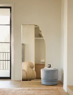 a large mirror sitting on top of a wooden floor next to a chair and ottoman