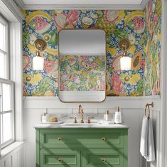 a bathroom with a green vanity and floral wallpaper on the walls, along with a gold framed mirror