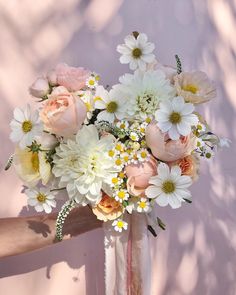 a bouquet of white and pink flowers in a vase on the arm of a woman