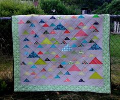 a quilt is hanging on a fence in the grass, with trees and bushes behind it