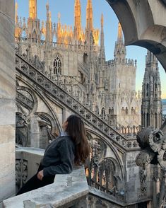 a woman sitting on top of a stone wall next to a building with spires