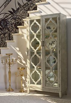 a white cabinet sitting next to a stair case with glass doors and ornate designs on it