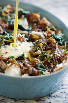 a blue bowl filled with mashed potatoes topped with spinach and cheese being poured into it