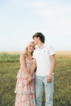 a young man and woman standing next to each other in a grassy field with tall grass