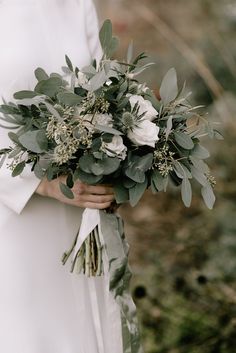 a woman holding a bouquet of flowers and greenery