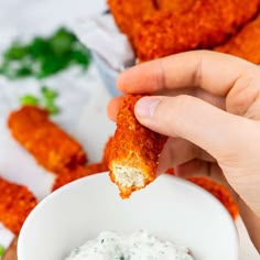 a person dipping something into a white bowl filled with ranch dressing next to fried chicken wings