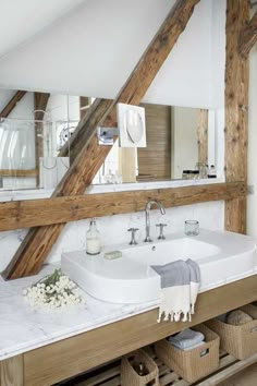 a white sink sitting under a large mirror in a bathroom next to a wooden beam