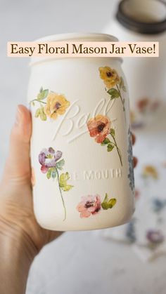 a hand holding a jar with flowers painted on it