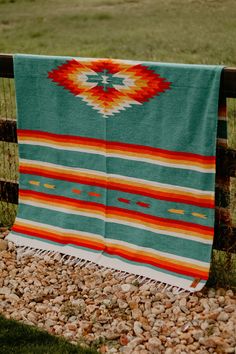 a blanket is hanging on a fence near rocks and grass in front of a grassy field