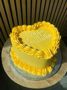 a yellow heart shaped cake with happy birthday written on the top and bottom, sitting on a wooden table