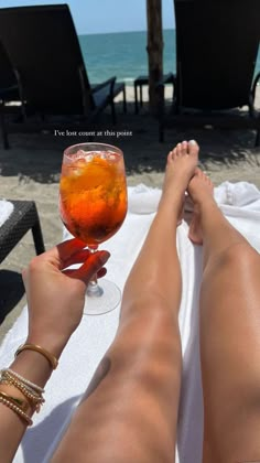 a woman's legs are shown holding a wine glass with orange liquid in it