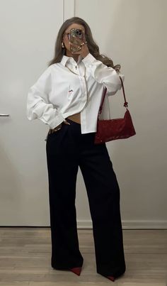 a woman in white shirt and black pants holding a red purse while standing next to a door