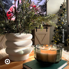 a candle is sitting on a table next to a book and a vase filled with greenery