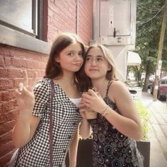 two young women standing next to each other near a brick building and holding coffee cups