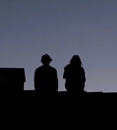 two people standing on top of a roof looking at the sky with a plane flying overhead