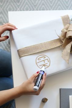 a woman is wrapping a gift with a brown ribbon and a white box that has a gold bow on it