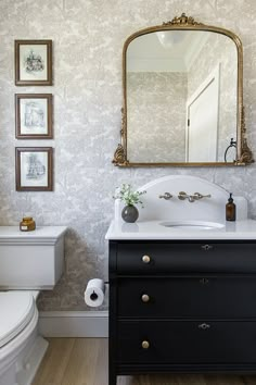 a white toilet sitting next to a black dresser in a bathroom under a large mirror