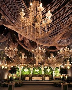 an indoor wedding venue with chandeliers and lights hanging from the ceiling, surrounded by greenery