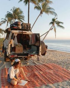 a woman sitting on top of a blanket next to an suv with luggage in the back