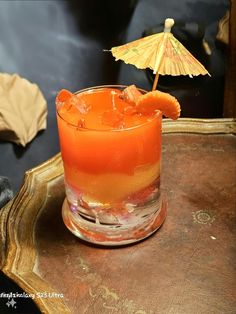 an orange drink sitting on top of a wooden table next to a yellow and white umbrella