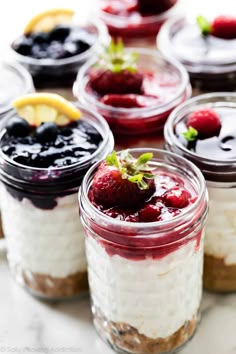 several desserts in glass jars with fruit on top