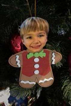 a young boy wearing a gingerbread christmas ornament hanging from a christmas tree