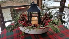 a candle is lit in a bowl with pine cones and berries on the table outside