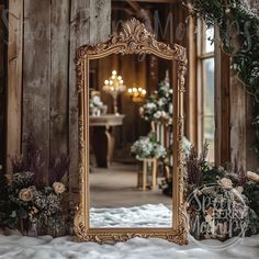 an ornate gold framed mirror sitting on top of a white bed next to flowers and greenery