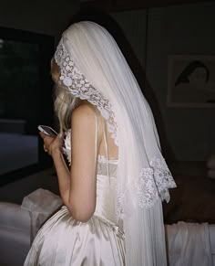 a woman in a wedding dress looking at her cell phone while she is wearing a veil