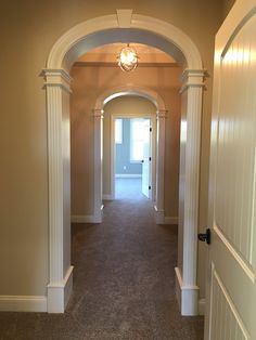 an empty hallway with white columns and light fixture on the ceiling, leading to another room