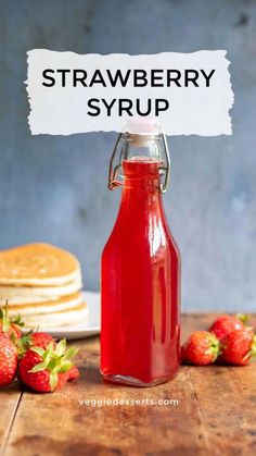 strawberry syrup in a glass bottle with strawberries around it on a wooden table next to pancakes