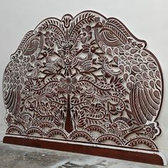 an intricately carved wooden panel depicting a tree with leaves and flowers on it, in front of a white wall