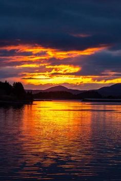 the sun is setting over water with mountains in the distance and clouds reflecting on the water