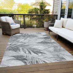 a large area rug on a wooden deck with white furniture and plants in the background