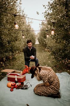 a man and woman sitting on a blanket in an apple orchard