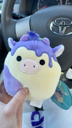 a hand holding a small stuffed animal in the middle of a car steering wheel area