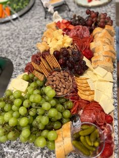 an assortment of cheeses, crackers and grapes on a platter with other snacks