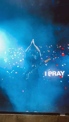 a man standing on stage with his hands up in the air while holding a guitar