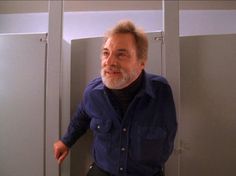 an older man standing in front of two metal lockers with his hand on the door handle