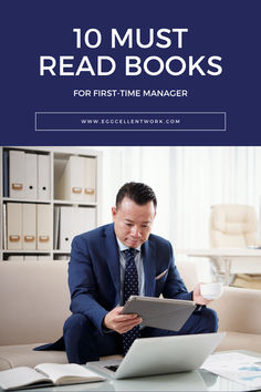 a man in a suit sitting at a table reading a book and holding a cup